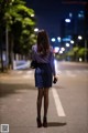 A woman in a purple shirt and blue skirt walking down the street.