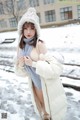 A woman in a white coat and hat standing in the snow.