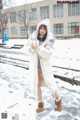 A woman in a white coat is standing in the snow.