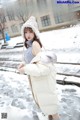 a woman in a white coat and hat standing in the snow