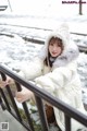 A woman in a white coat and hat leaning against a railing.