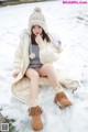 A woman sitting in the snow wearing a white coat and hat.