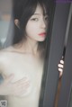 A naked asian woman looking out of a window.