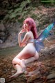 A woman with pink hair and a fairy wings sitting in the water.