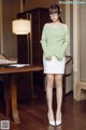 A woman in a green sweater and white skirt posing for a picture.