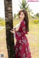 A woman in a red dress leaning against a palm tree.