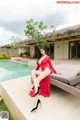 A woman in a red dress sitting on a lounge chair by a pool.