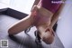 A woman in a pink sports bra and shorts crouching on the floor.