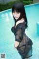 A woman in a black dress standing next to a swimming pool.