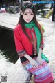 A woman in a red jacket and green scarf sitting on a stone wall.