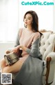 a woman sitting on a chair wearing a pink sweater and grey skirt