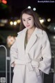 A woman in a white coat standing in front of a fence.