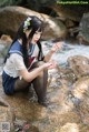 A woman in a school uniform sitting on a rock by a stream.