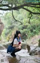 A woman in a school uniform sitting on a rock by a stream.