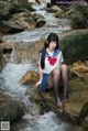 A woman in a sailor outfit sitting on a rock by a stream.