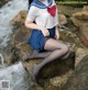 A woman in a sailor outfit sitting on a rock by the water.