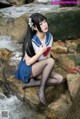 A woman in a sailor outfit sitting on a rock by a stream.