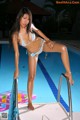 A woman in a blue bikini standing on the edge of a swimming pool.