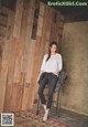 A woman sitting on a stool in front of a wooden wall.