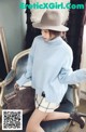 A woman sitting on a chair wearing a blue sweater and a hat.