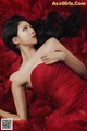 A woman in a red dress laying on a bed of red roses.