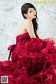 A woman in a red dress sitting in front of a wall of paper flowers.