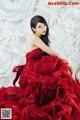 A woman in a red dress sitting in front of a wall of paper flowers.