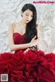 A woman in a red dress sitting in front of a wall of paper flowers.