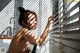 A naked woman standing in front of a window with blinds.