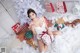 A woman sitting on a bed with presents under a Christmas tree.