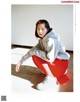 A woman in a gray sweatshirt and red pants crouching on the ground.