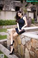 A woman in a black dress sitting on a stone wall.