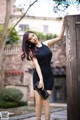 A woman in a black dress leaning against a wooden fence.