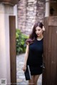 A woman in a black dress leaning against a wooden door.