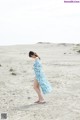 A woman in a blue dress walking on a sandy beach.