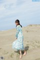 A woman walking on a sandy beach in a blue dress.