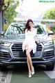 A woman in a white dress sitting on the hood of a car.