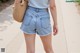 A woman wearing a blue top and denim shorts.